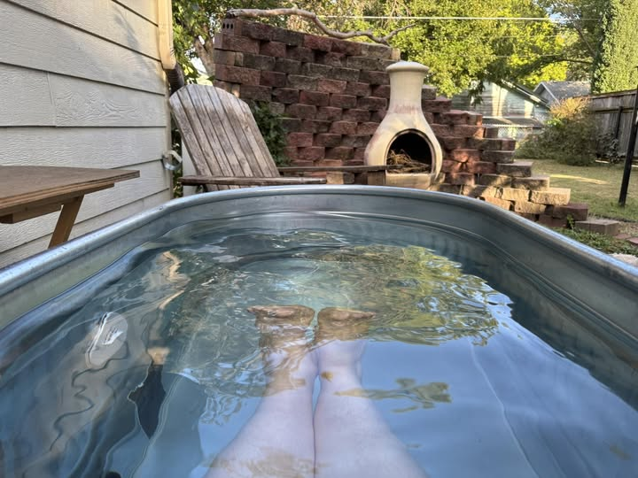 A photo taken from the perspective of someone sitting in a tank pool, with legs extended in the water and a chiminea at the foot of the tub